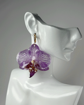 Preserved purple orchid earring dipped in resin in a face-shape ceramic display.