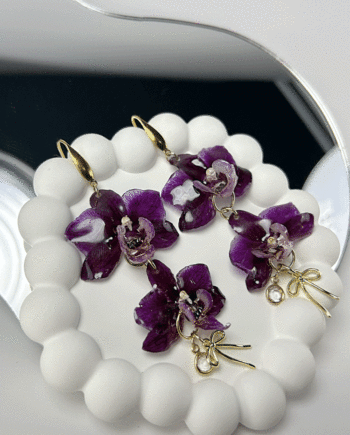 Preserved purple double orchid earrings dipped in resin, in a white ceramic display.